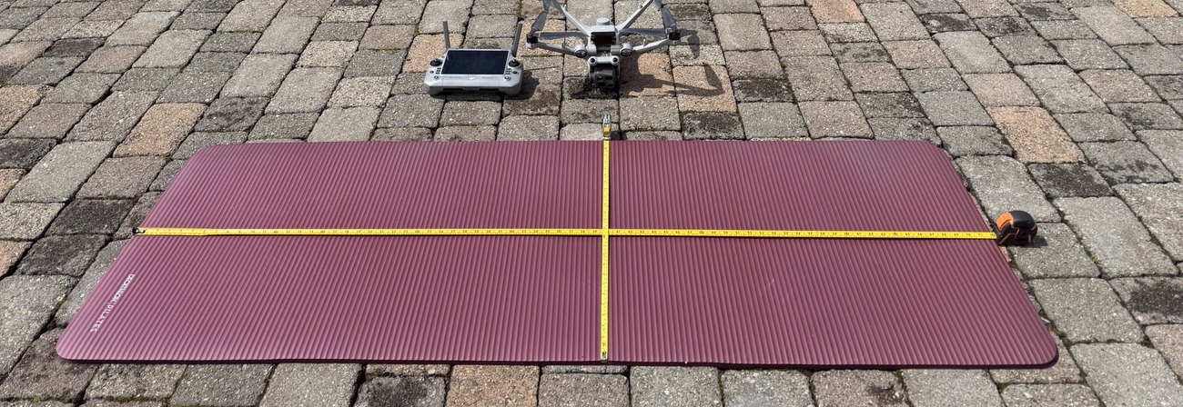 DJI Matrice 4 beside a flat calibration target with a tape measure laid across it on paving